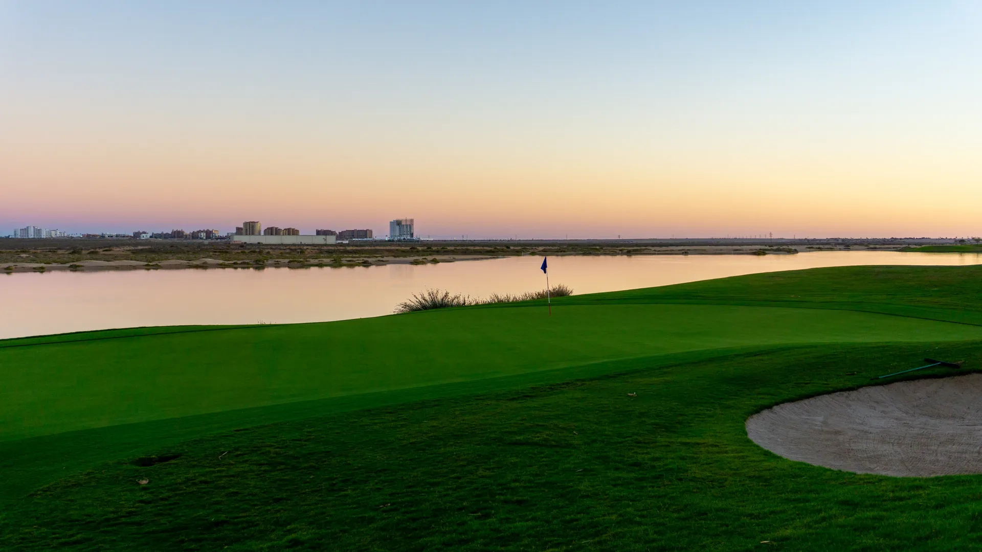 Golf green and flag beside a tranquil lagoon at dusk