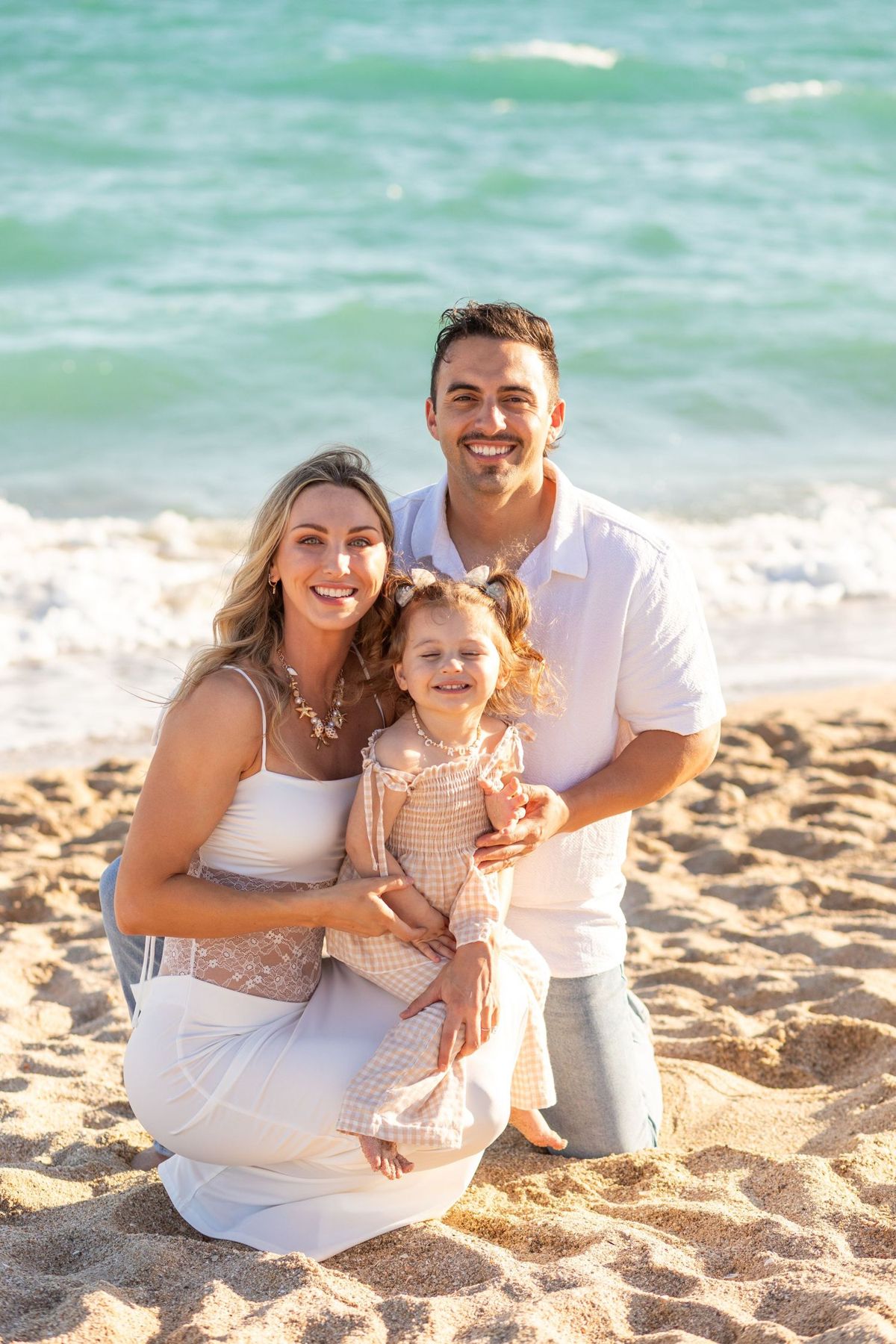 Parents and their daughter posing beside turquoise water on a Rocky Point beach
